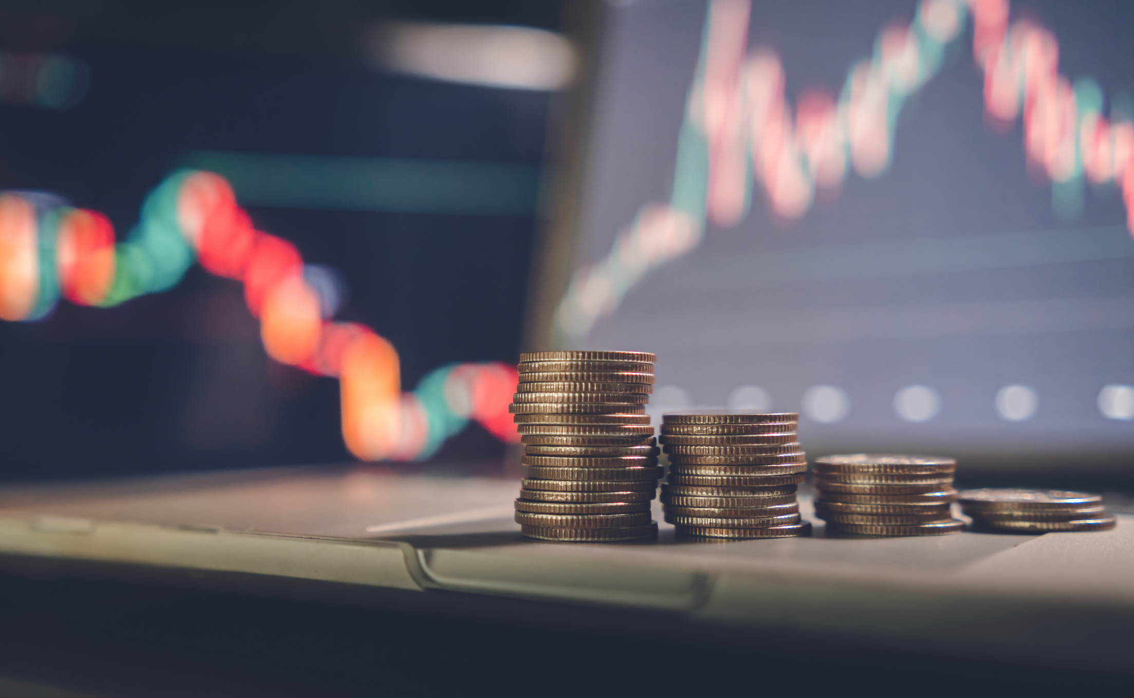 Stacked coins with a background monitor showing data graphs.