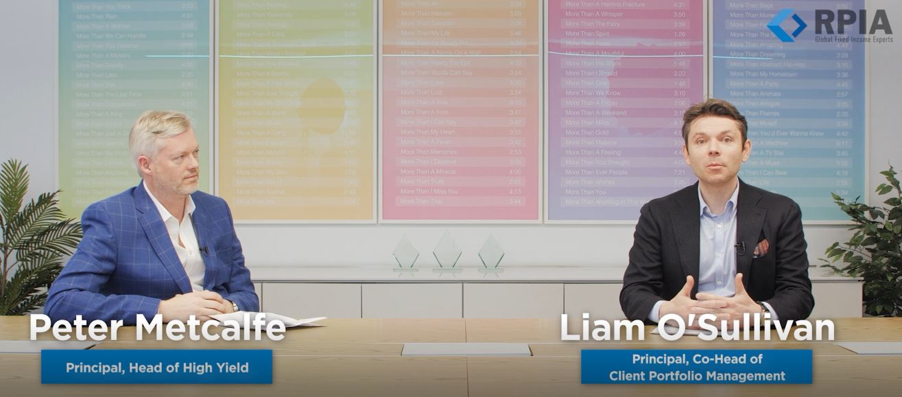 Peter Metcalfe and Liam O'Sullivan talking at a boardroom table with colourful artwork in the background